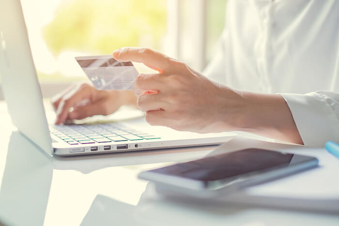 Close up of hands holding a credit card paying a bill online with laptop