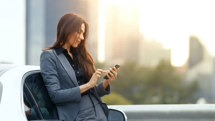 Businesswoman leaning on car and looking at phone